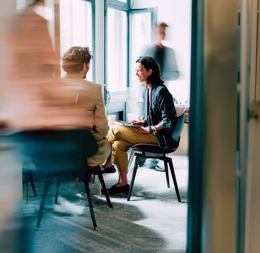Colleagues in a meeting room, one taking notes while another listens